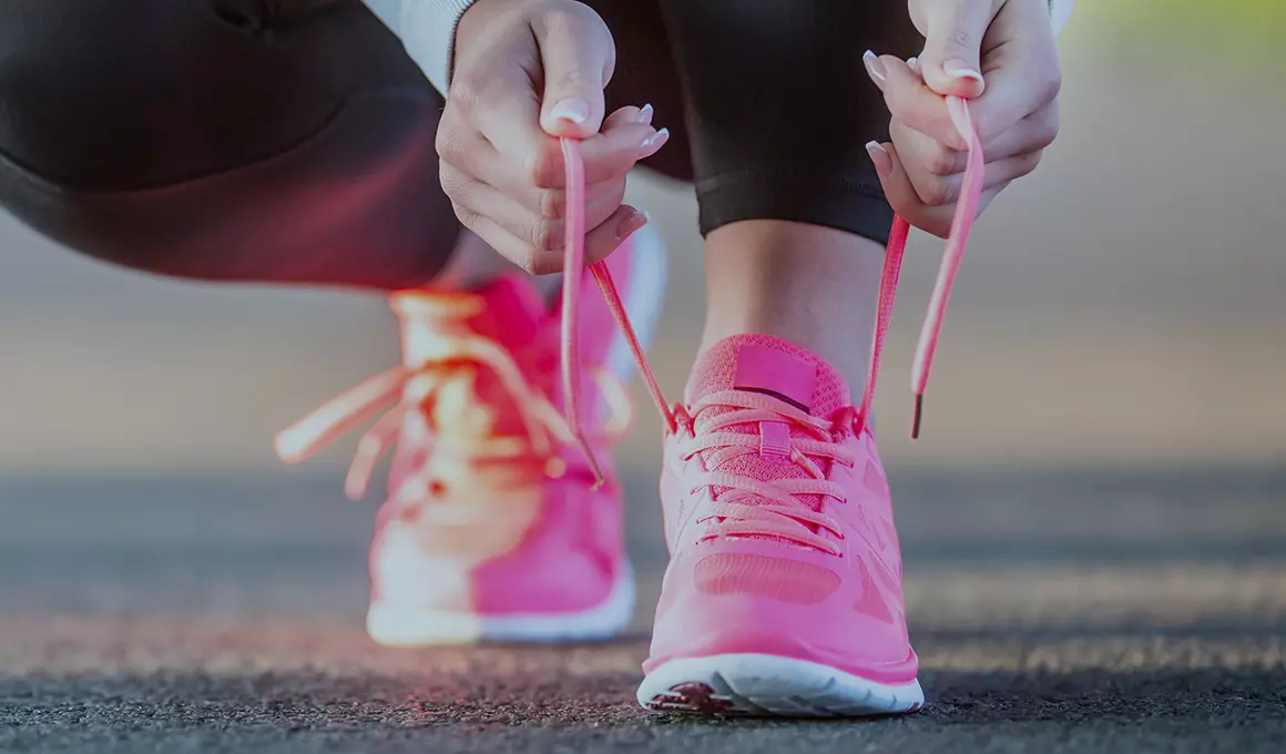 Female crouching down tying the laces on bright pink running shoes