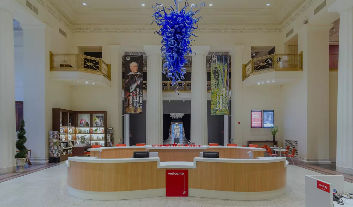 The welcome desk in the lobby at the Cincinnati Art Museum sits below a blue Chihuly sculpture hanging from the very tall ceiling.