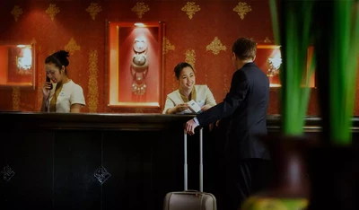 Two receptionists sit behind the welcome counter in an IHG hotel. One is speaking on the phone while the other smiles at an unrecognizable customer.